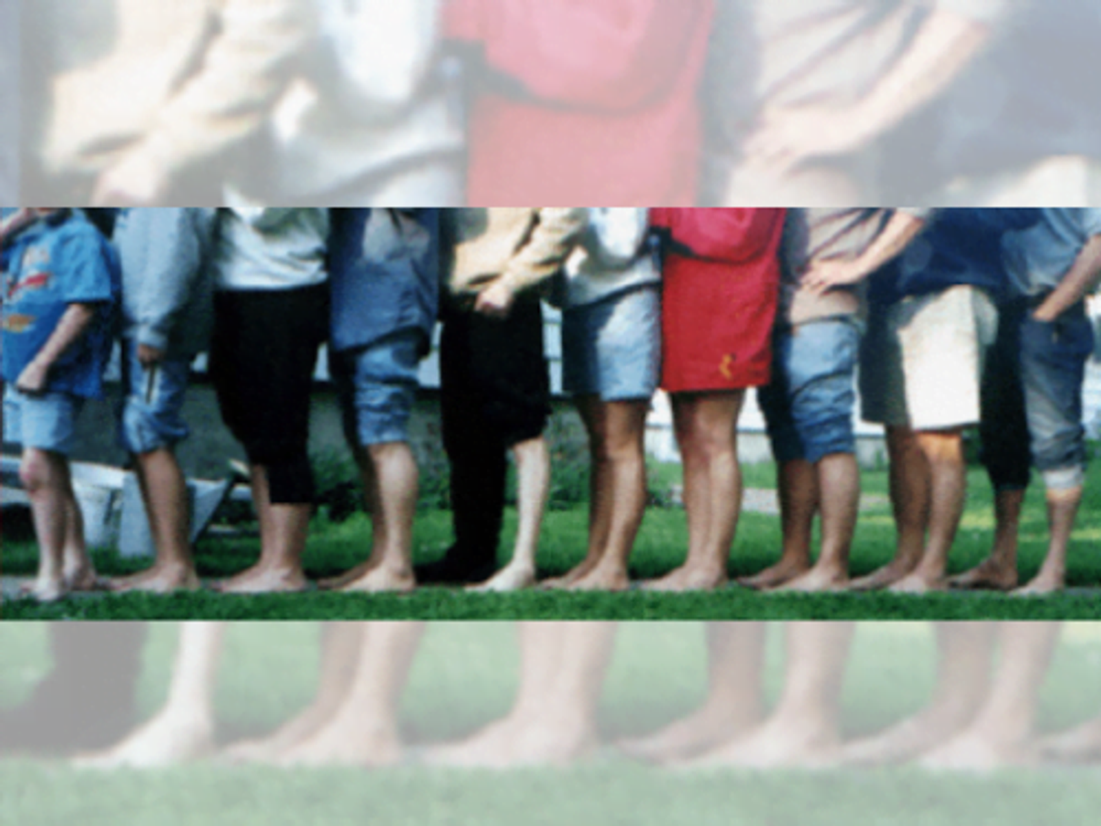 Group of children standing in a line on grass, wearing casual clothing and shoes.