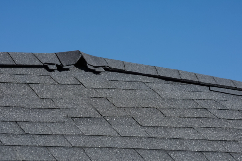 Ridge cap running along the top of a grey shingle roof under a blue sky