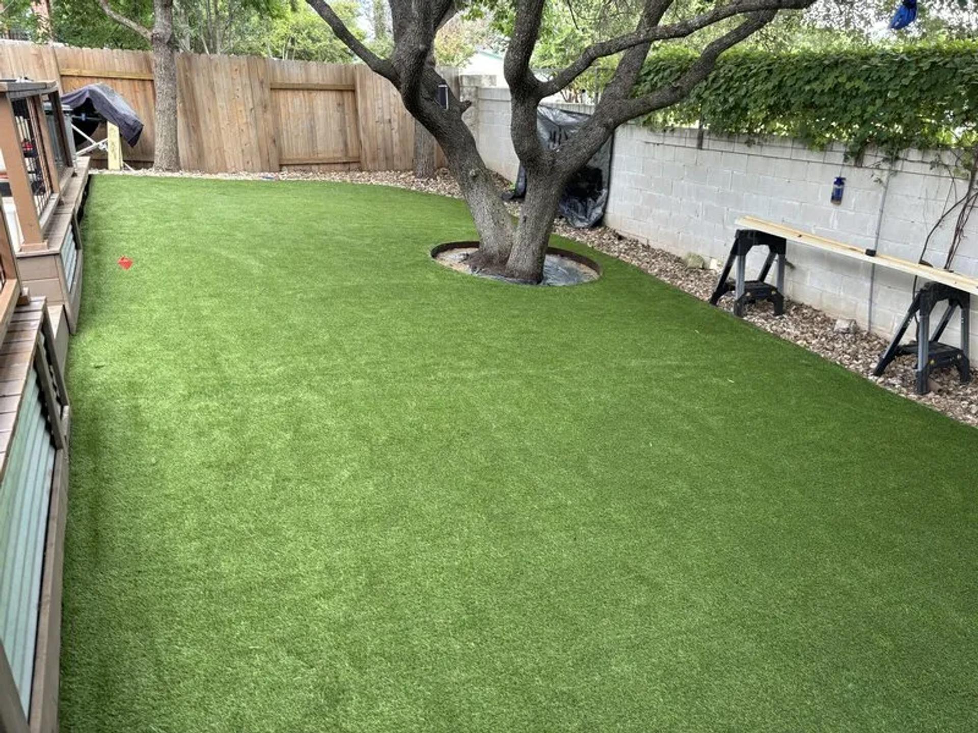 A backyard with artificial turf and one tree