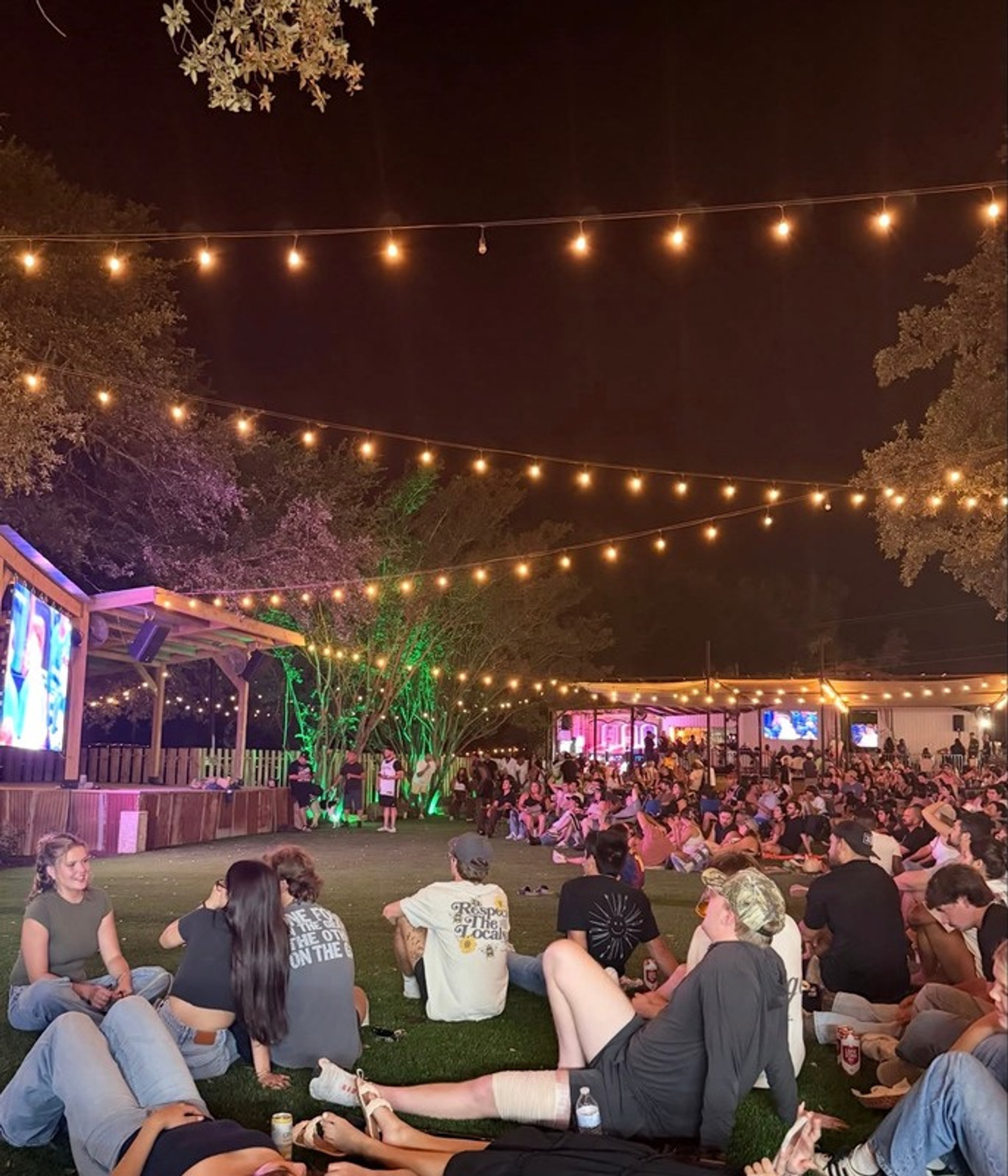 Crowd relaxing on the turfed lawn at The Lucky Duck under string lights
