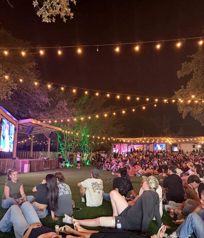 Crowd relaxing on the turfed lawn at The Lucky Duck under string lights