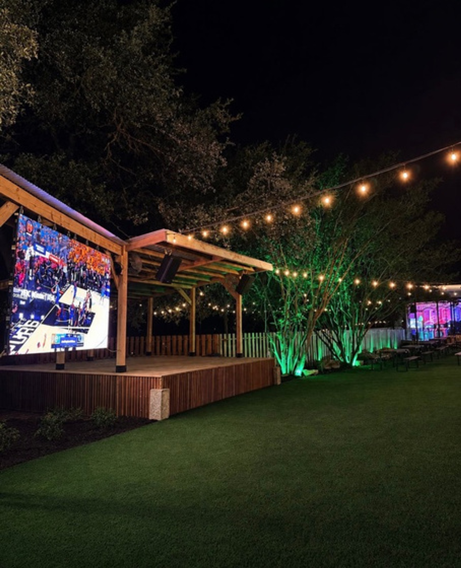 The Lucky Duck patio with artificial turf and a big screen lit up at night