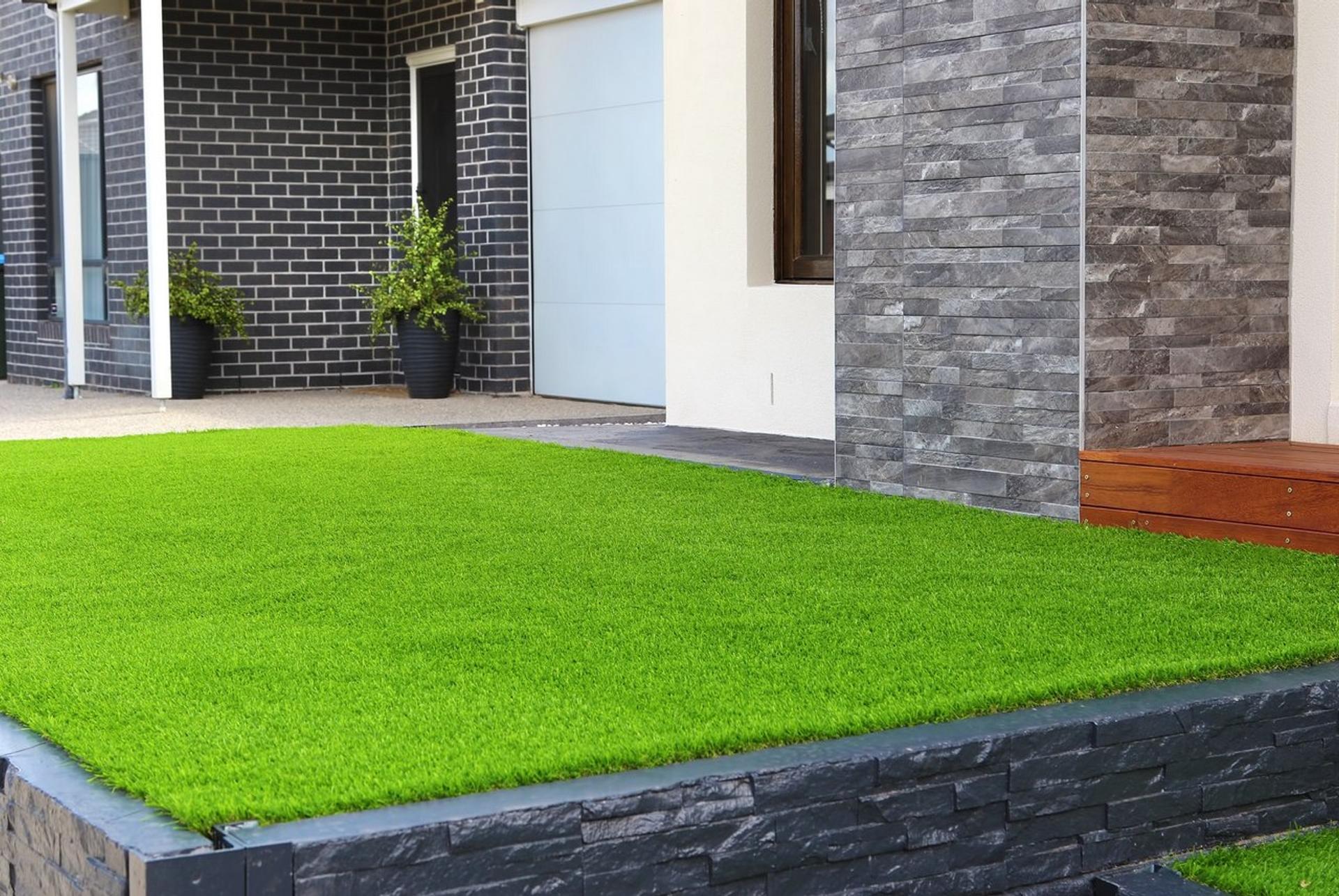 Modern front yard with bright artificial turf and black stone edging in front of a contemporary home