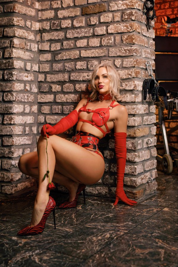 Nahaufnahme Domina Josy Rose hockend vor Backsteinwand – BDSM-Fetisch & Dirty Games in Köln.