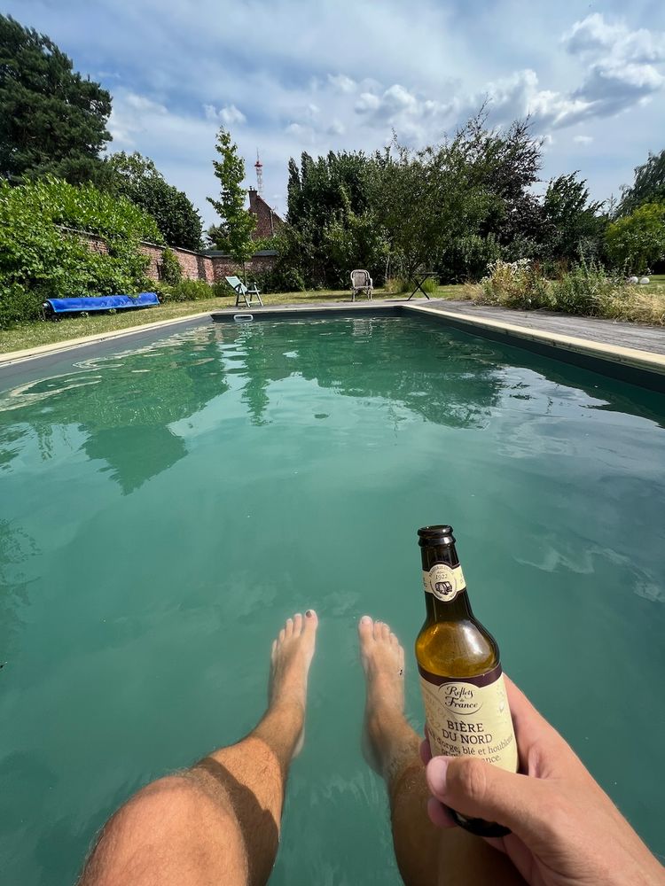 man with feet in pool with beer