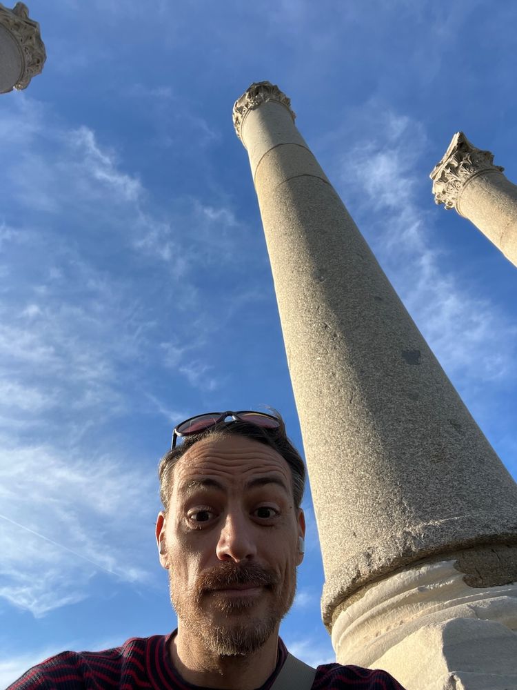 man taking selfie below ancient ruin