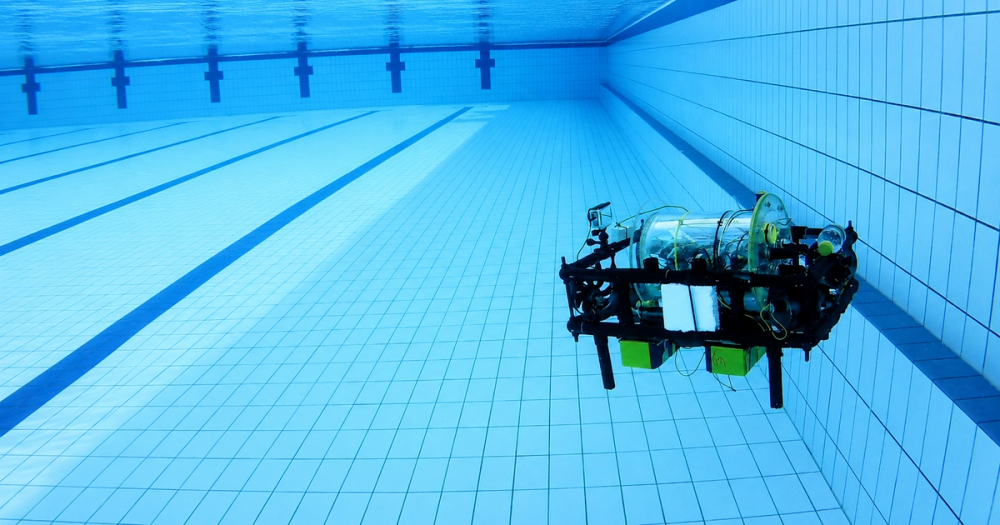 BRACU Duburi floating mid-water in an empty swimming pool lane during a test run, its black frame and clear cylindrical enclosure visible against the blue tiles