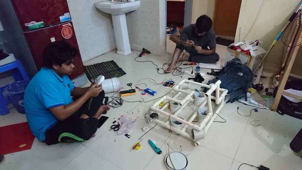 Adnan, in a blue t-shirt, and Arko working on electronics beside the PVC rover frame