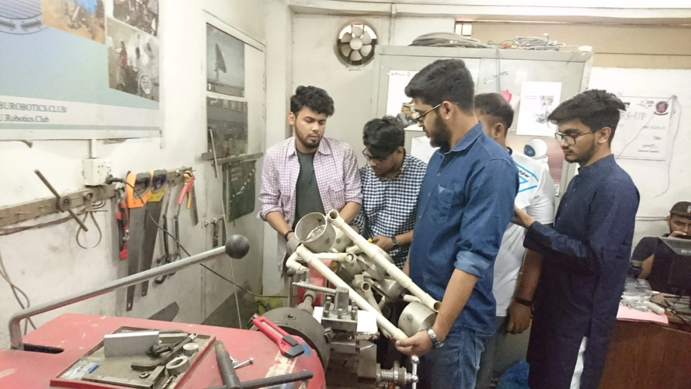 Riyad, Farabi, and Muntasir attaching joints on a PVC structure while Elham holds it steady, in the mechanical lab
