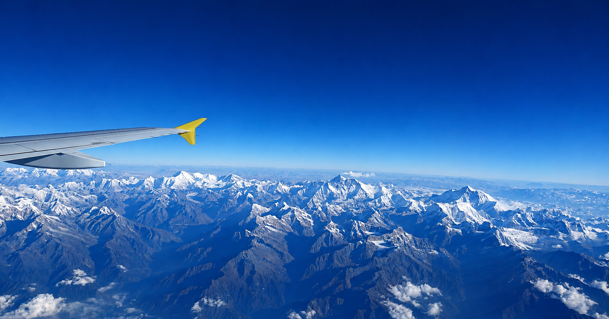 View from an airplane wing over Bhutan’s snow-covered Himalayan mountains under a clear blue sky.