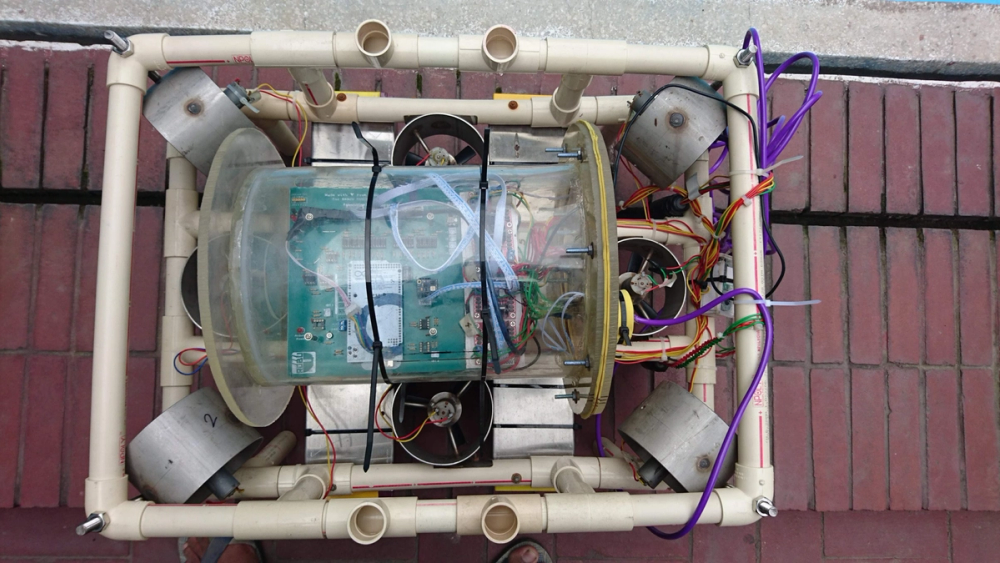 Top-down view of BRACU Duburi's final PVC frame, with four thrusters and a clear cylindrical enclosure housing the control PCB and wiring