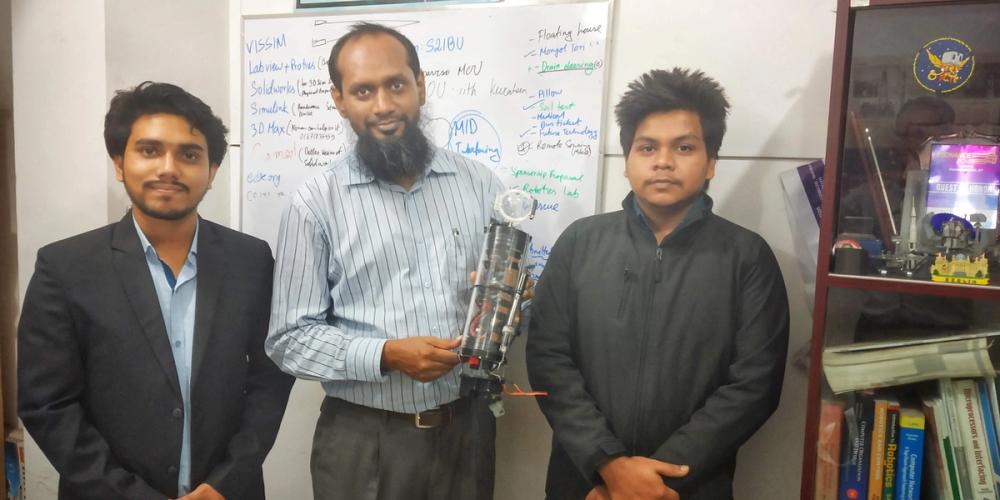 Adnan and a teammate with their thesis advisor, holding the CanSub underwater sensing capsule in front of a whiteboard.