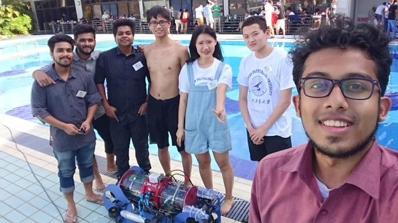 BRACU Duburi team members posing poolside with students from a Chinese university team wearing Northwestern Polytechnical University shirts, their robot in front