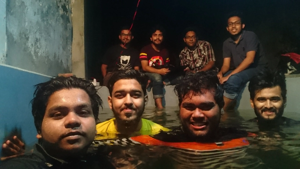 Part of the Duburi team, some in the water and some sitting on the edge, at their makeshift swimming pool at night