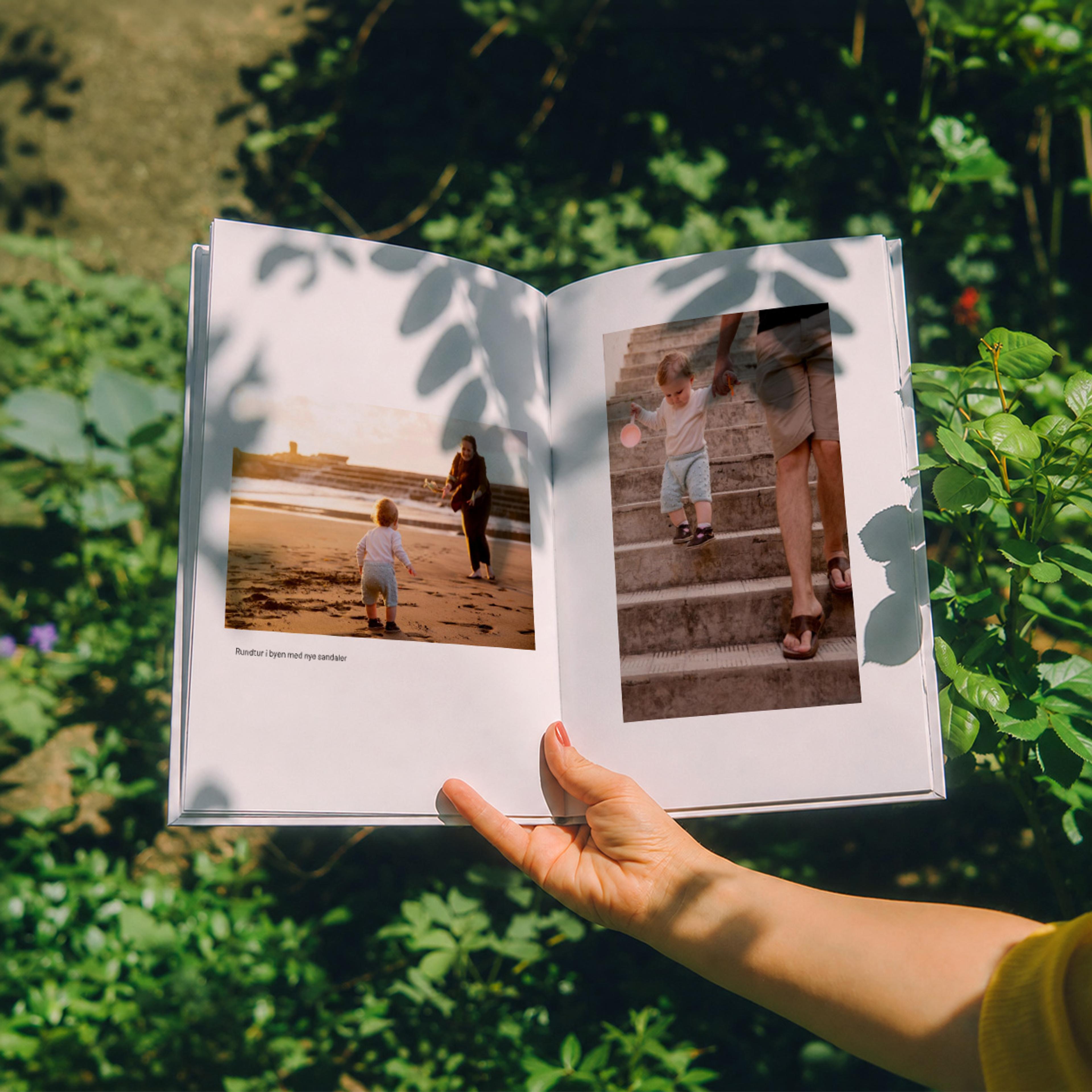Fotobok i stående format som holdes opp ute foran en busk, laget hos Elite Foto
