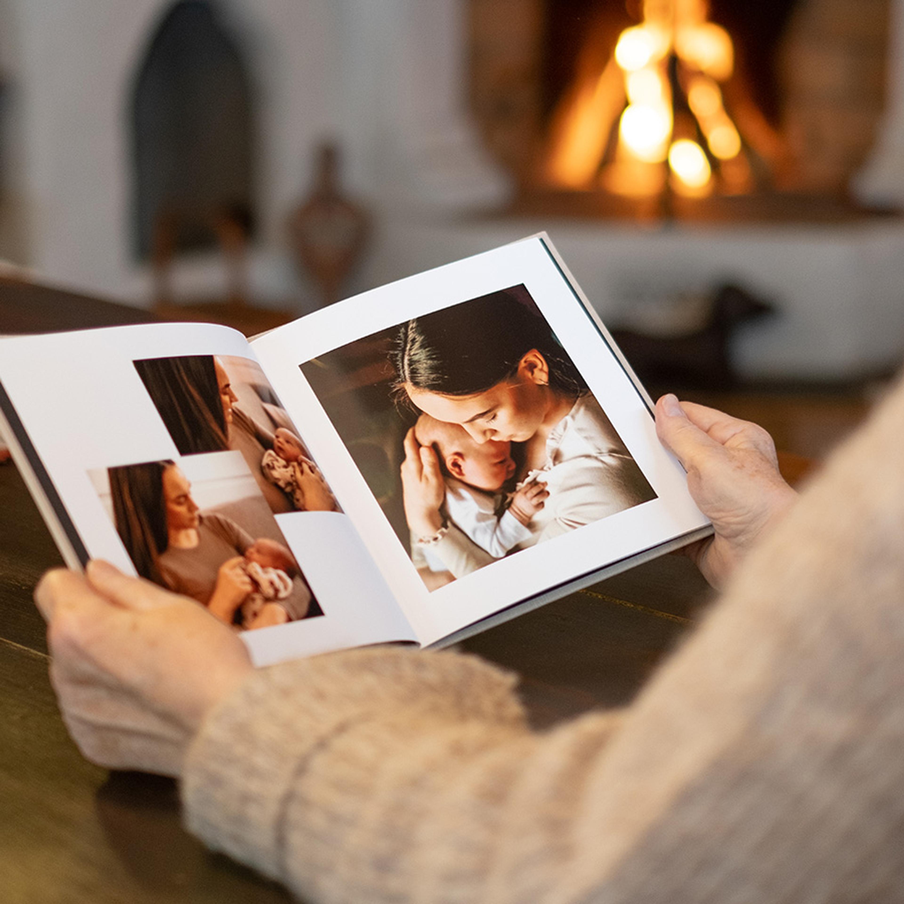 Dame ser i fotobok foran peisen