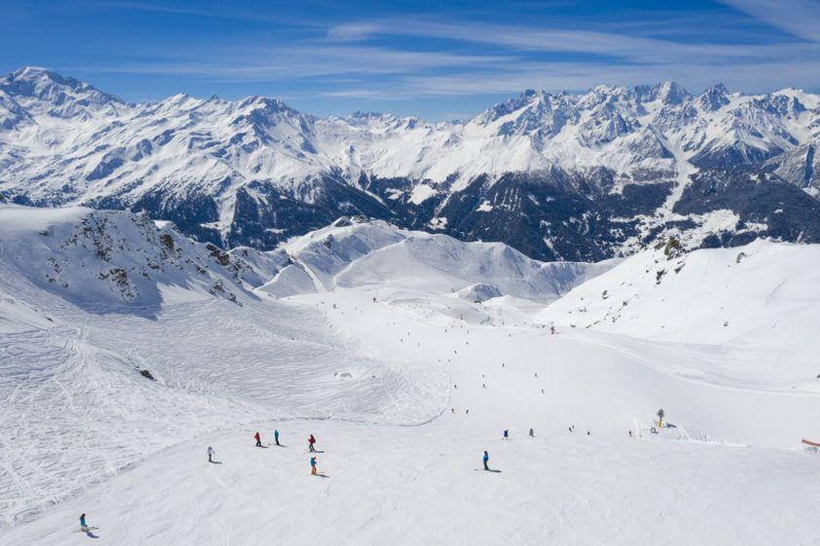 Aerial view of skiers on a piste in Verbier with blue skies and mountain peaks behind