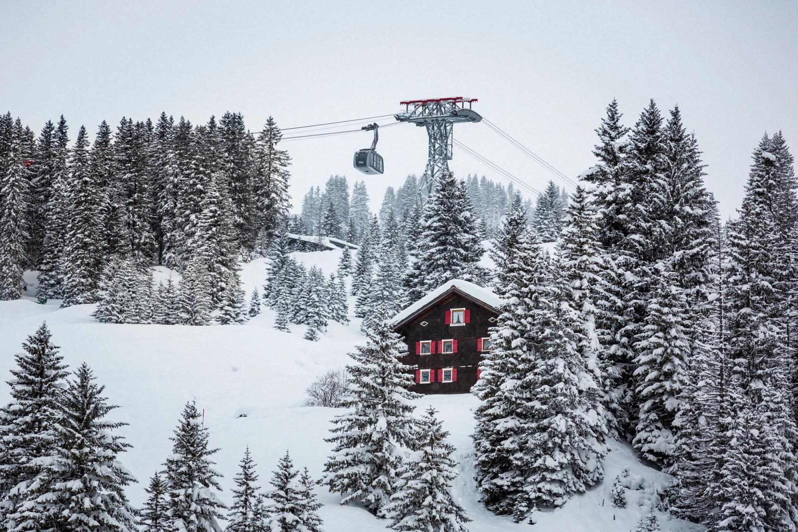 View over a traditional chalet and a cable car through an alpine forest in Lech