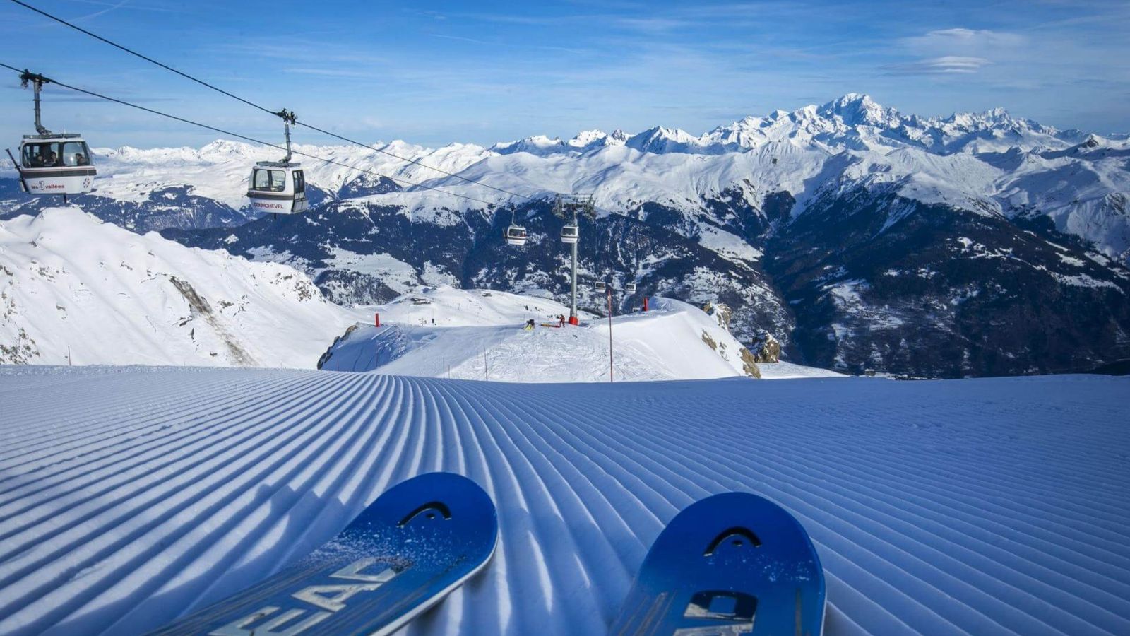 Tips of skis pointing down a groomed piste, with mountain views and a Courchevel gondola behind