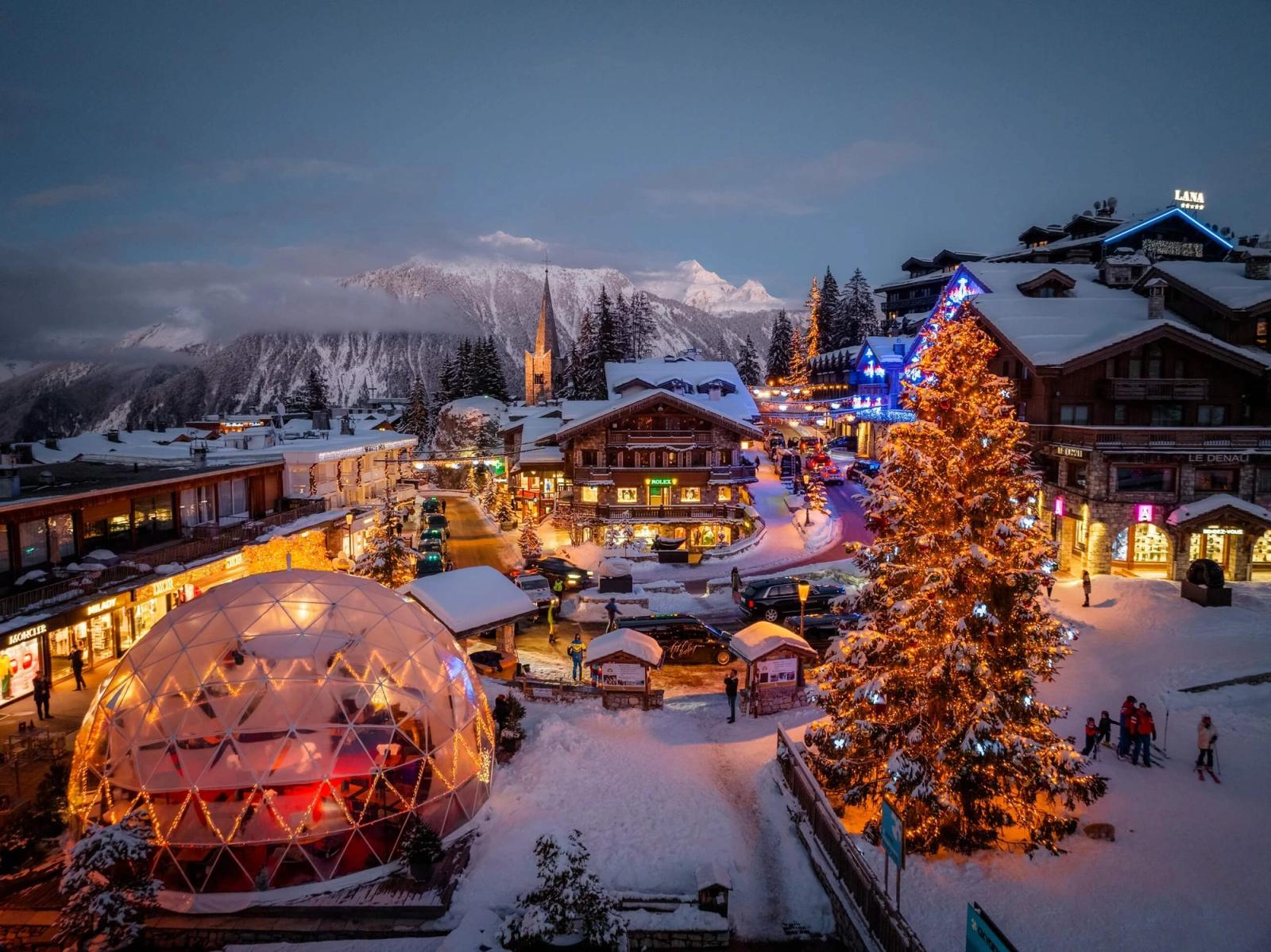 Festive fair at night in Courchevel, with a Christmas tree, stalls, and church spire behind