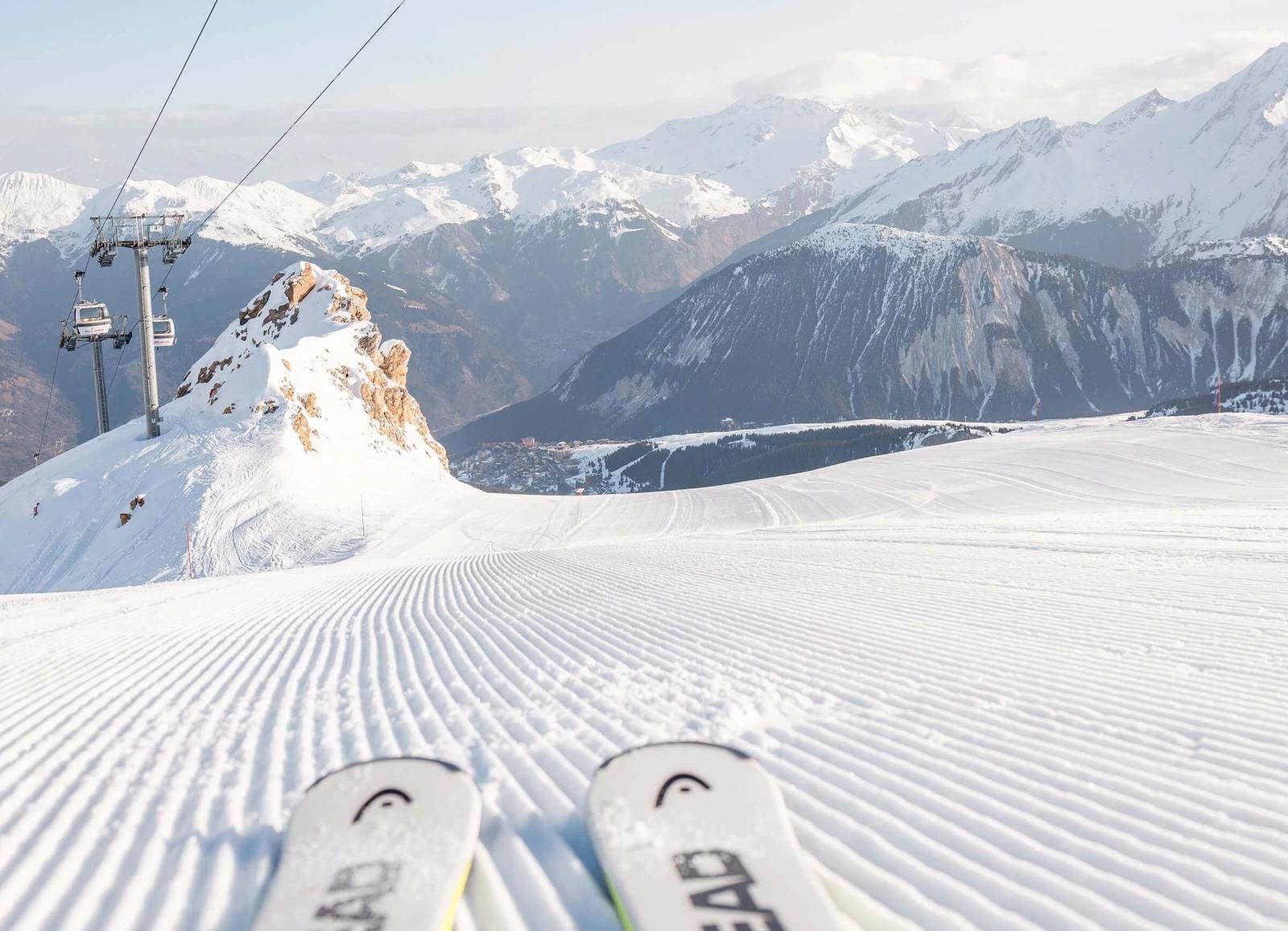 Point of view of a skier looking down the piste in Courchevel, with gondolas and mountains