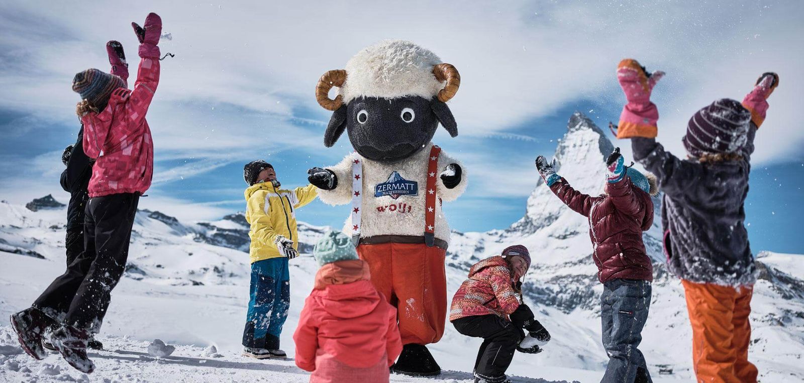 Wolli mascot with children around him throwing snow in the air
