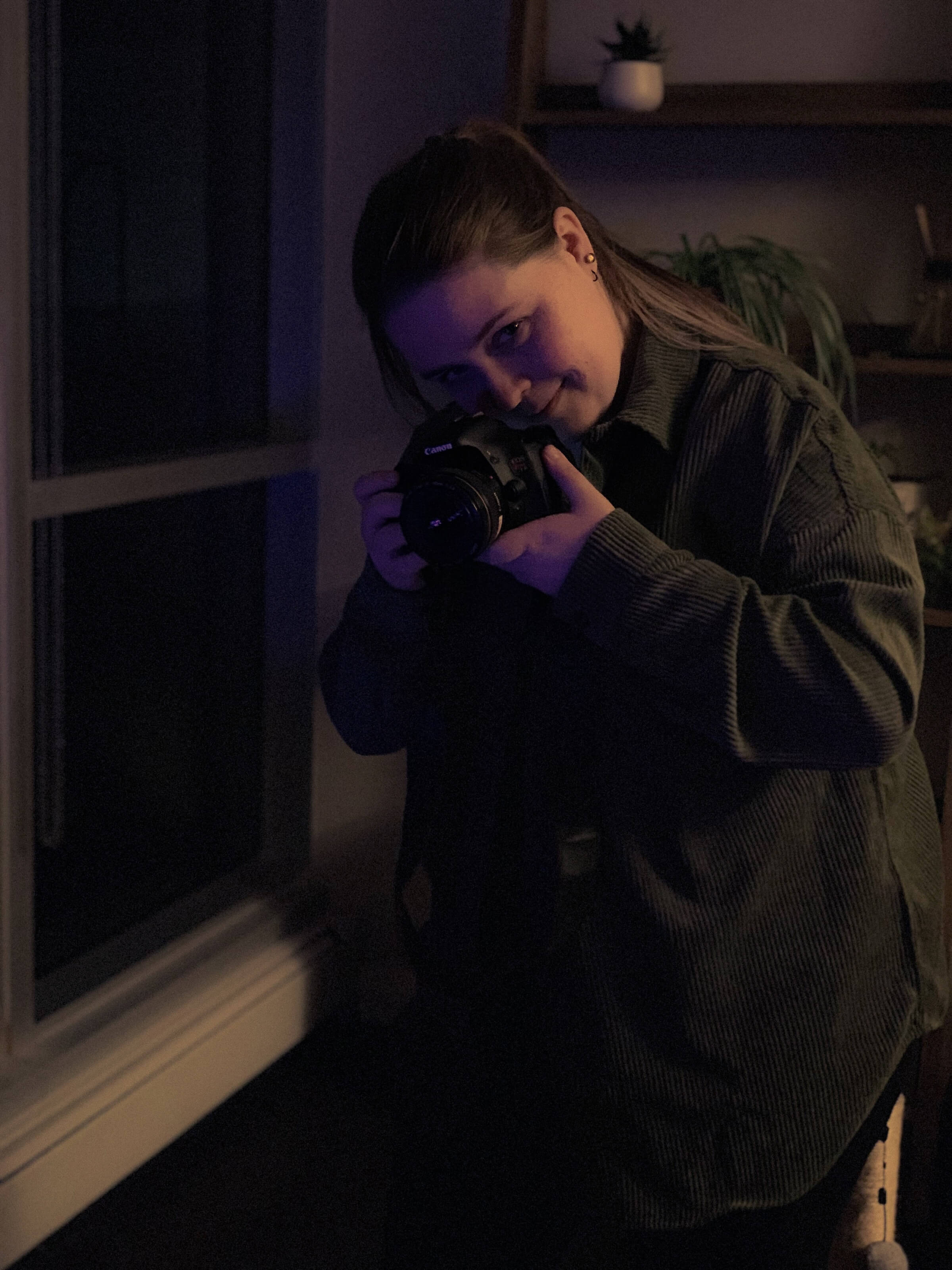 Headshot of Katie Struck in a dark room, holding a camera