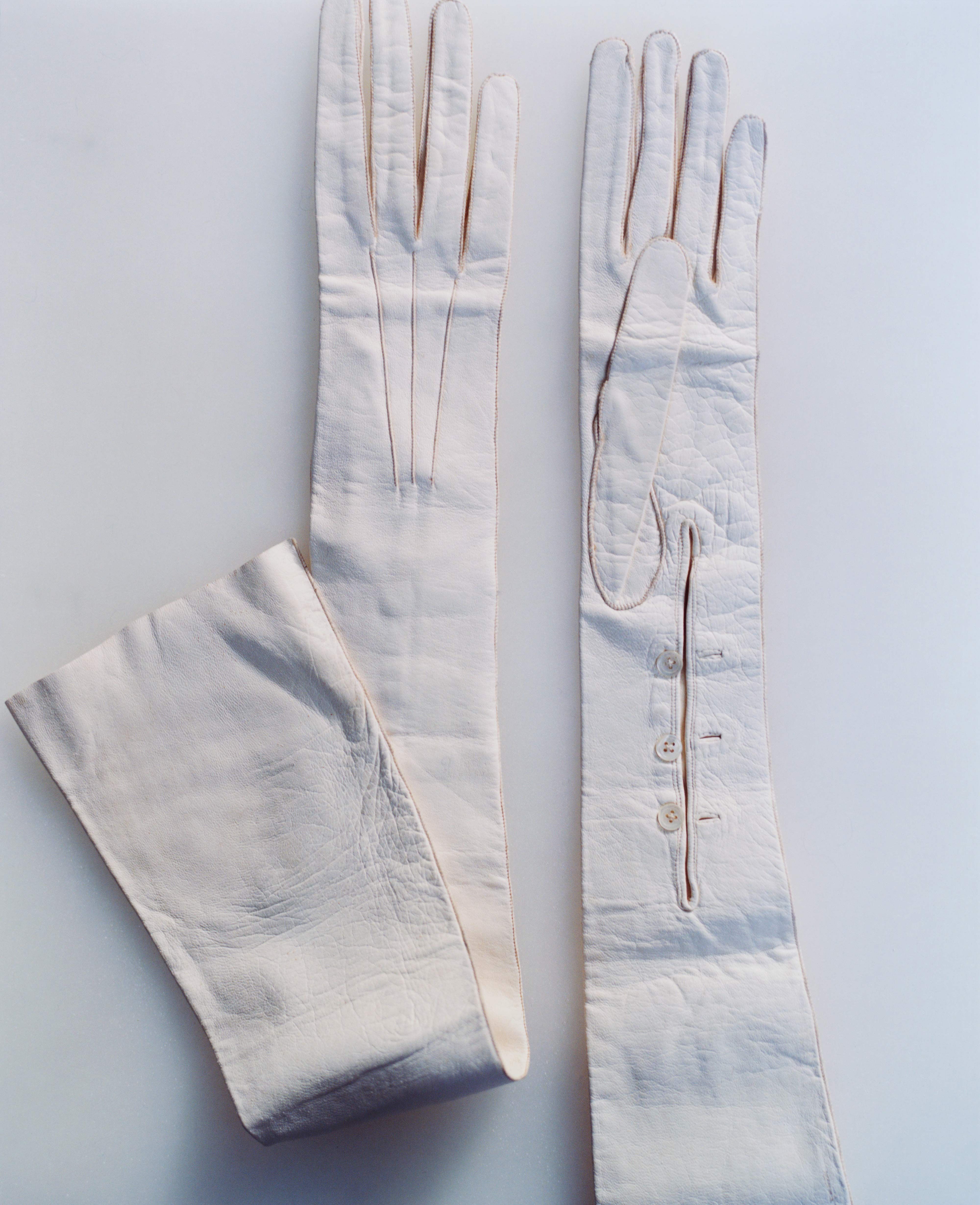 Pair of ivory, opera-length gloves laid flat, with a three-button wrist placket and stitched detailing on a light background.