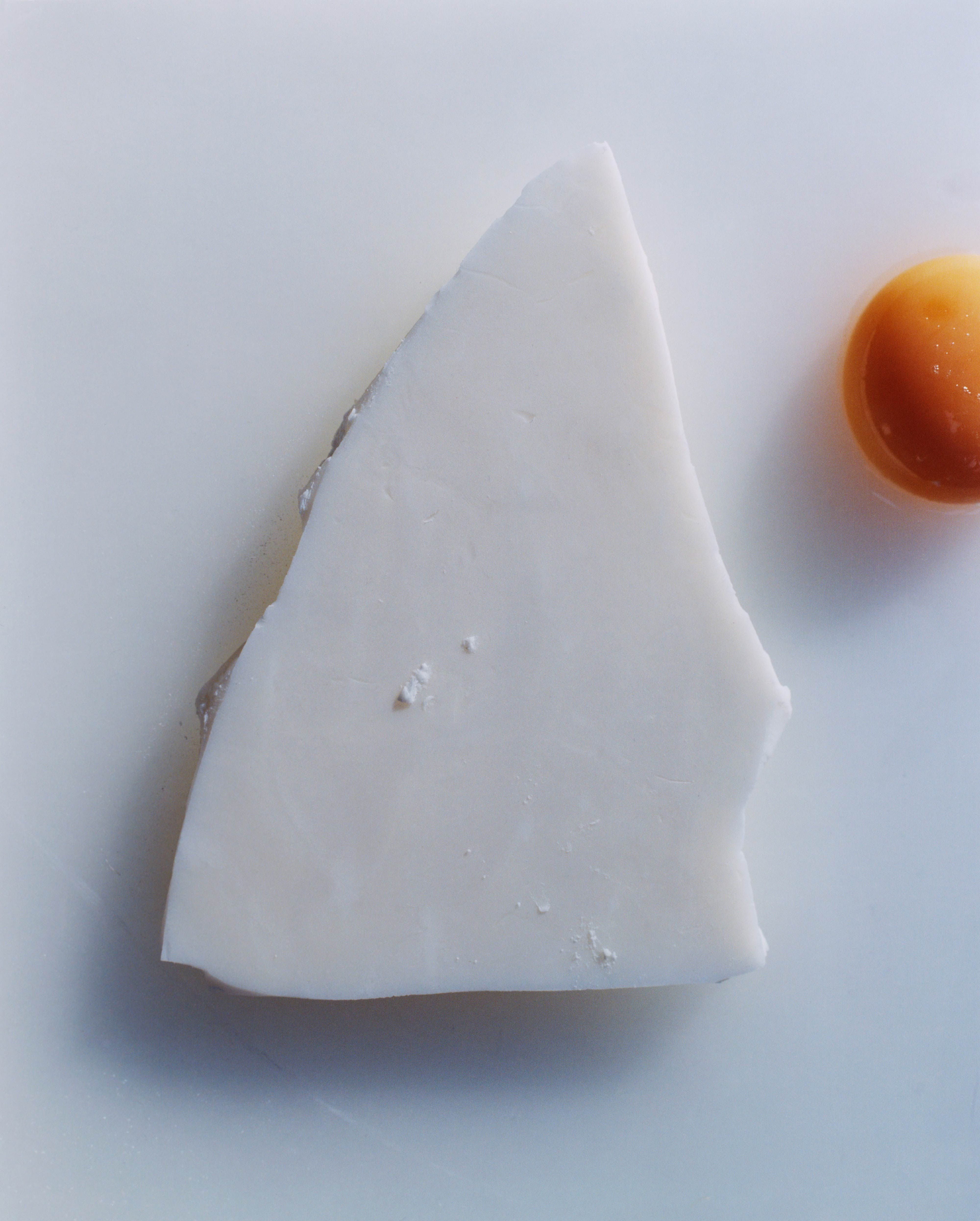 Minimal still life of a triangular ivory slab on a pale surface with a glossy amber droplet at the edge.