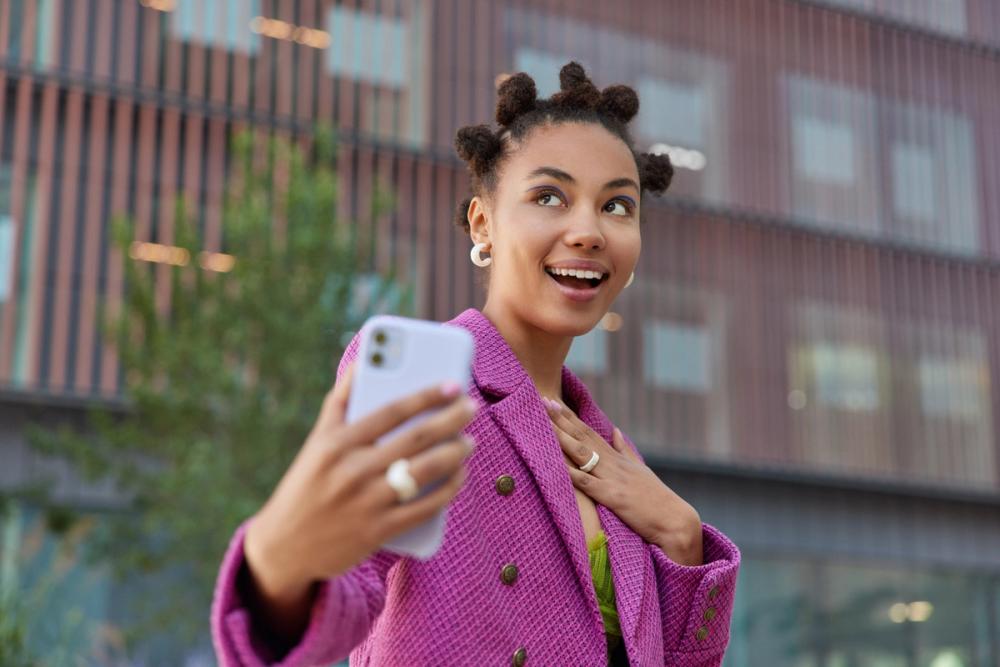 happy-dreamy-woman-with-funny-hairstyle-makes-photo-herself-wears-fashionable-pink-jacket-looks-somewhere-positively-poses-outdoors-against-blurred-background-technology-urban-lifestyle.jpg
