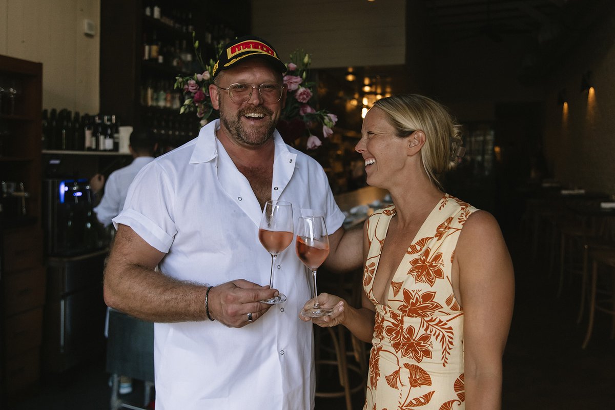 Chef Brian and a guest in a floral dress laugh together over glasses of rosé at the marble bar