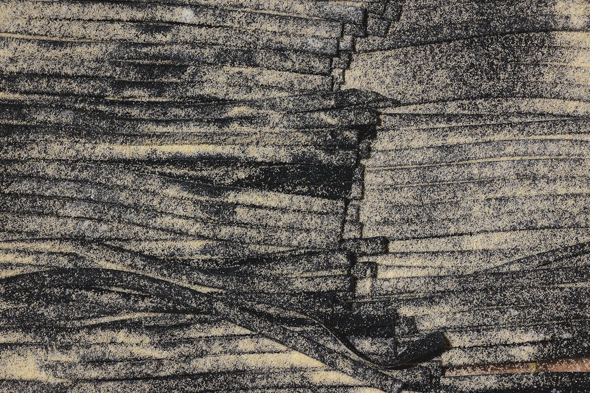 A close-up of hand-cut squid ink pasta strands, dusted with semolina flour