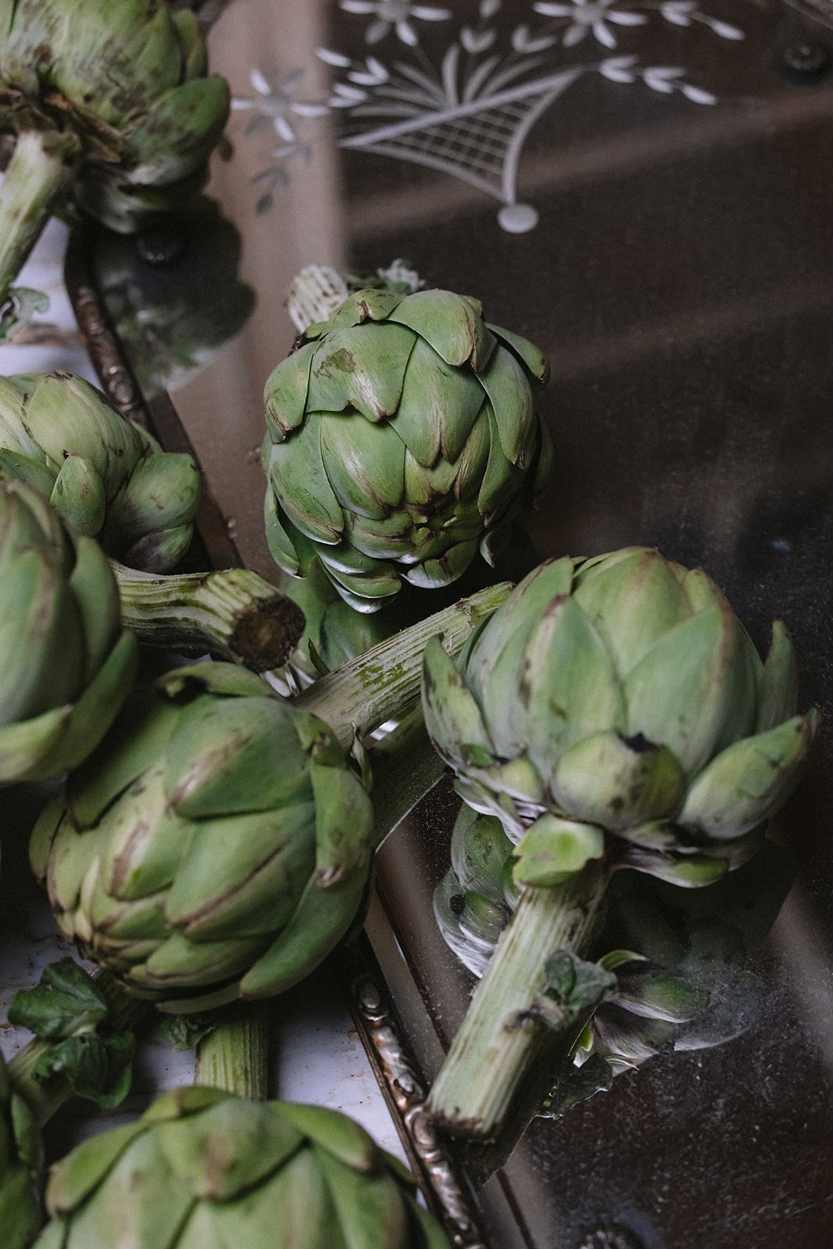 Fresh artichokes with their stems still attached, reflected in an antique etched mirror