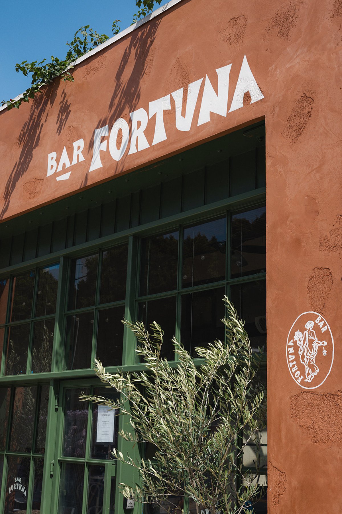 Bar Fortuna's terracotta exterior with painted signage, an olive branch, and the goddess emblem on Main Street, Santa Monica