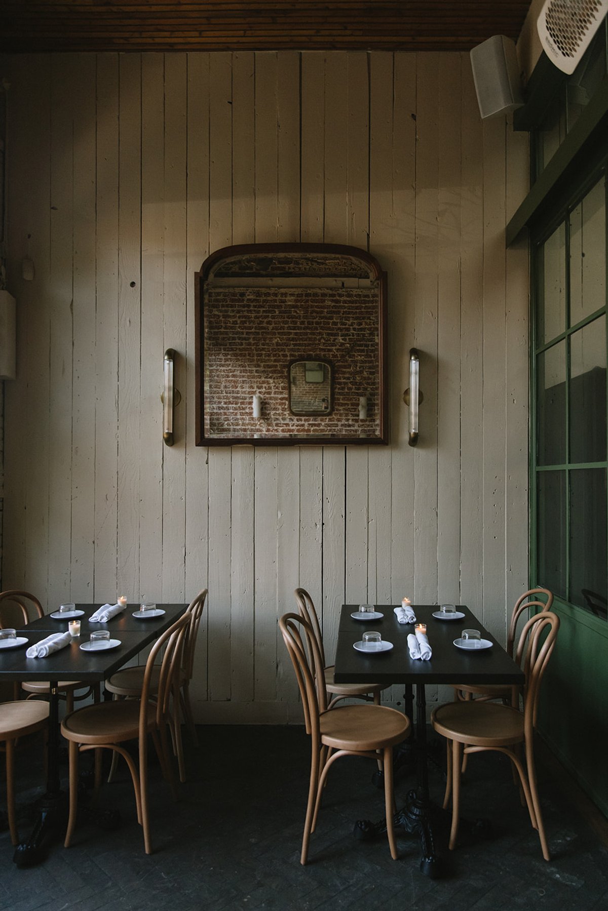Two candlelit dining tables set against a wood-paneled wall beneath a vintage mirror