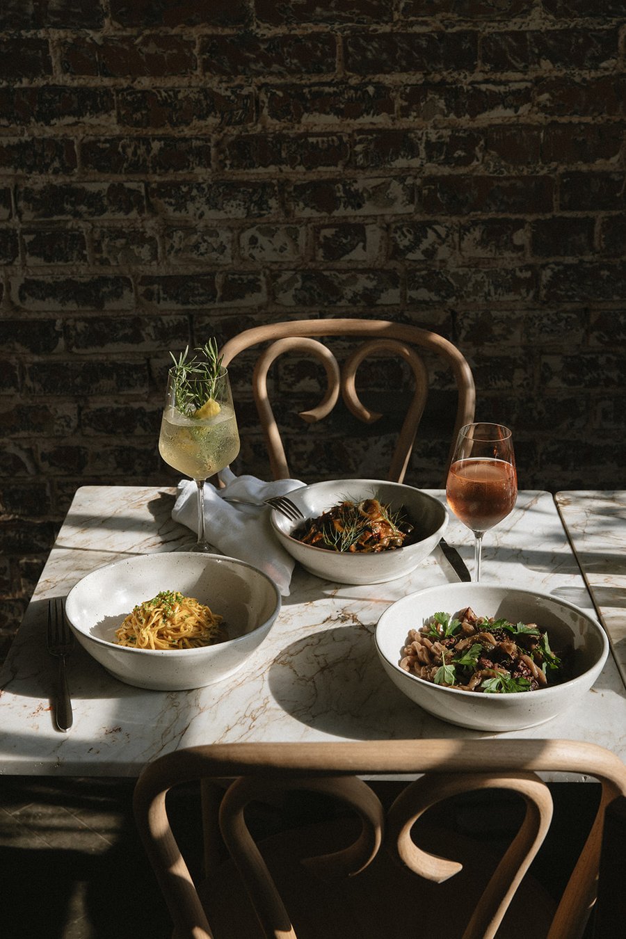 Bowls of pasta and a glass of rosé set on a marble table in the dining room