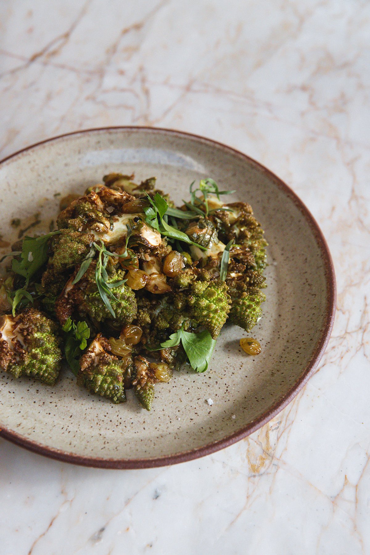 Roasted romanesco topped with herbs and golden raisins on a ceramic plate