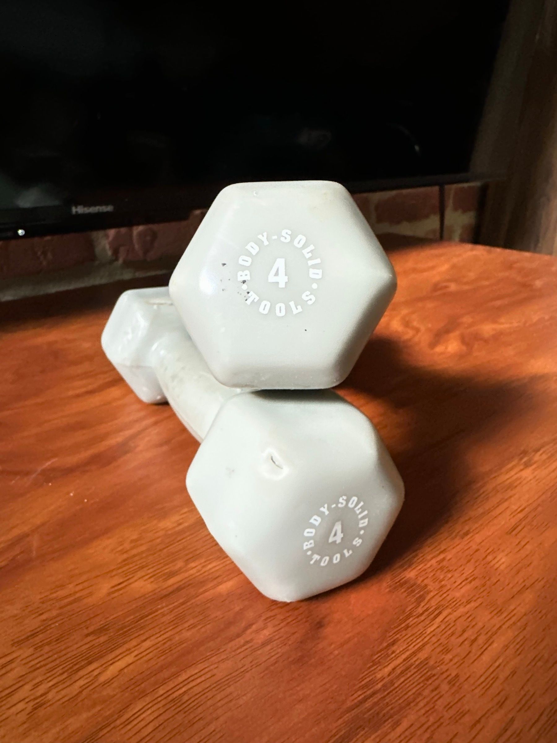 A pair of grey Body-Solid 4 lb hex dumbbells on a wood table.