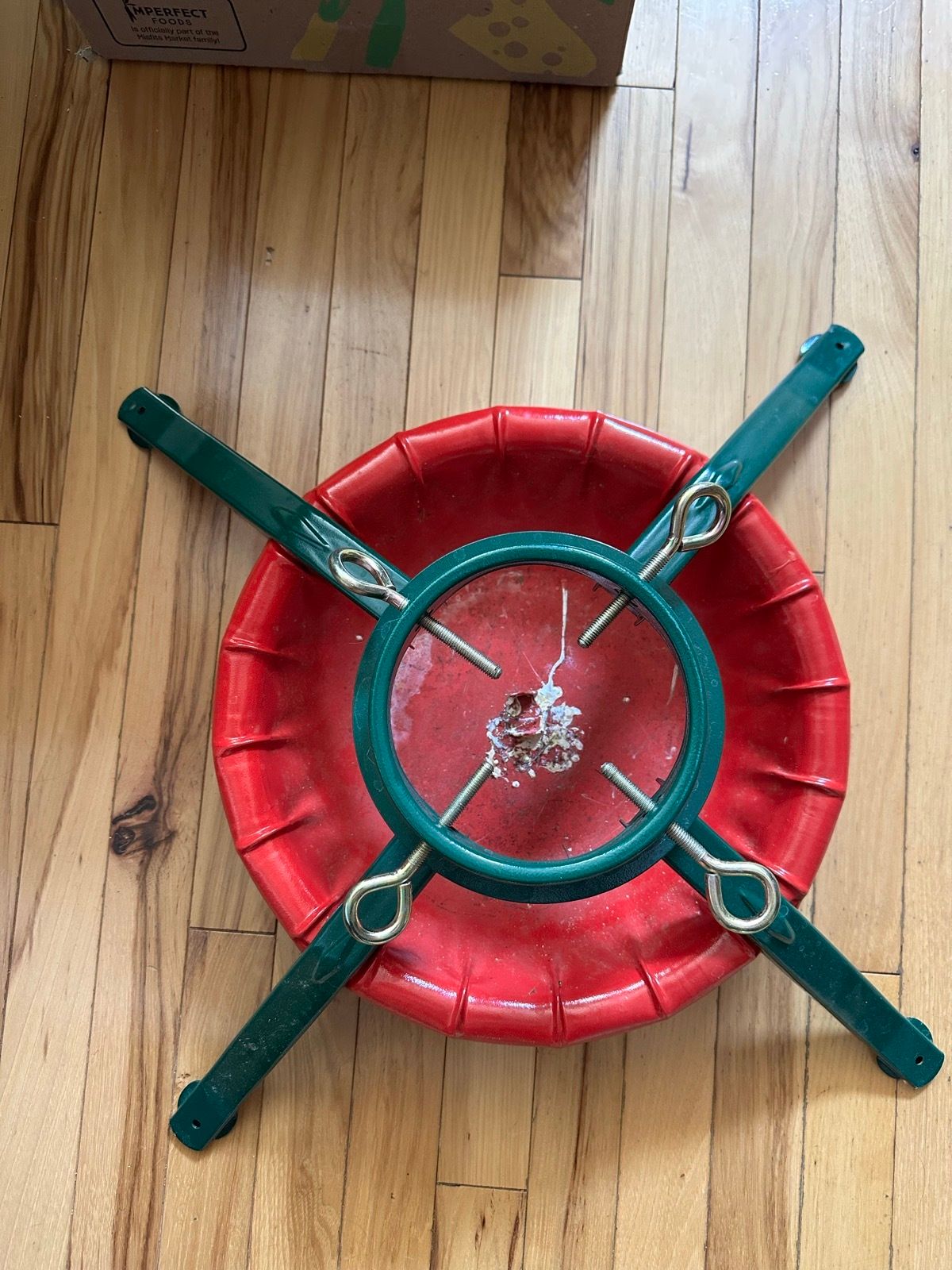 Red and green plastic Christmas tree stand with bolt clamps and a water reservoir.