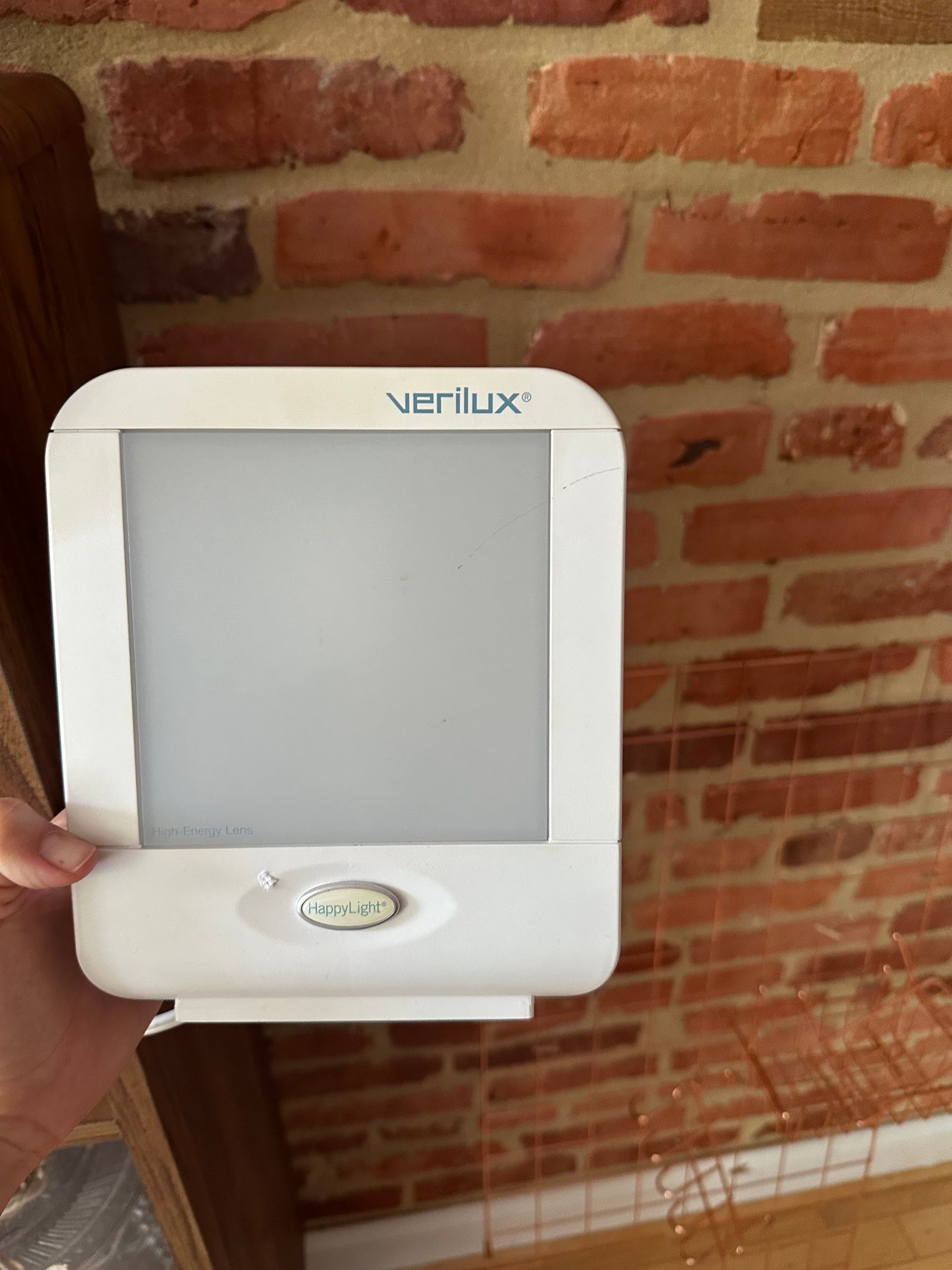 Verilux HappyLight full-spectrum light therapy lamp, white, held up against a brick wall.