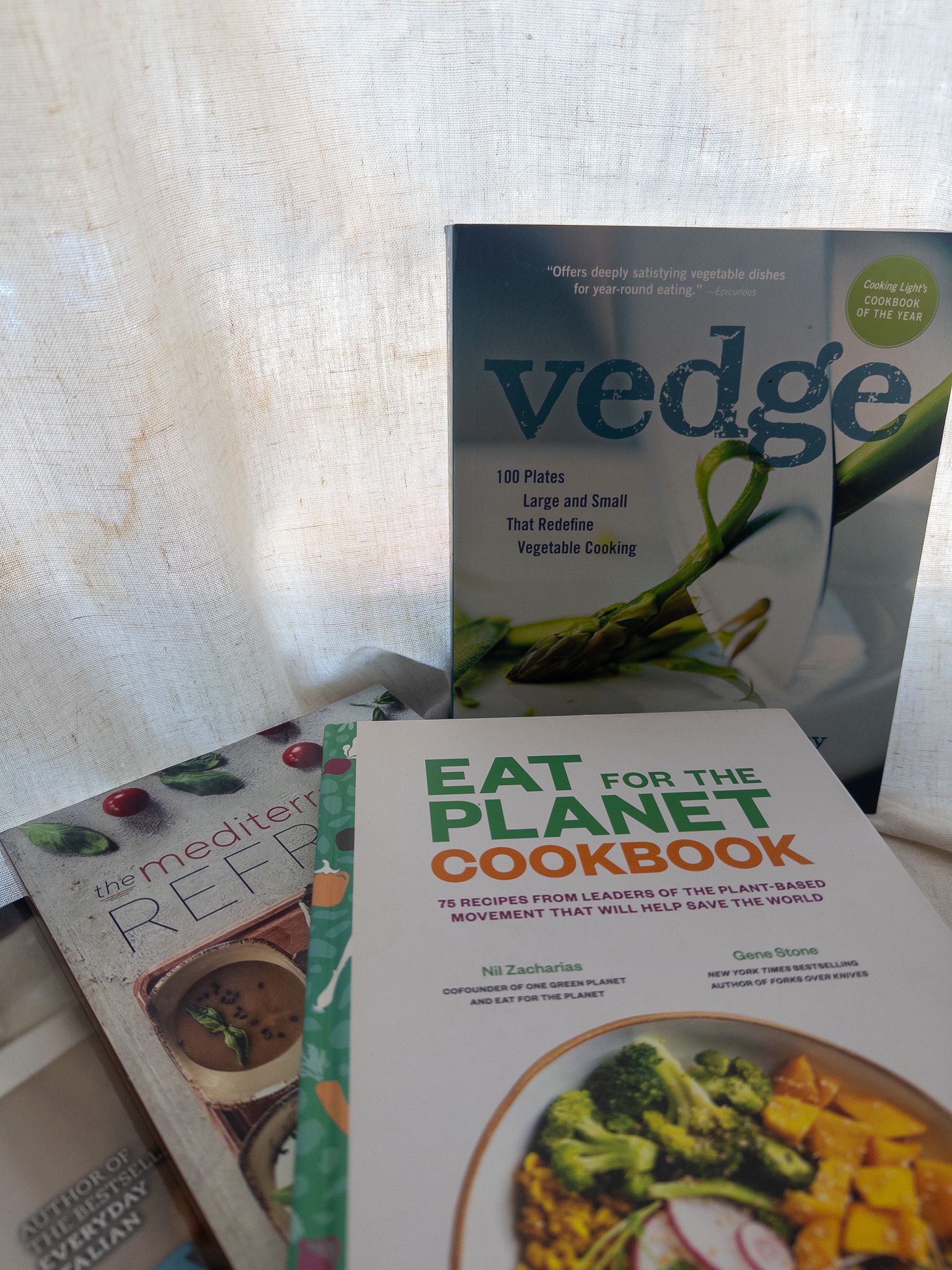 A stack of plant-based cookbooks including Vedge and the Eat for the Planet Cookbook.