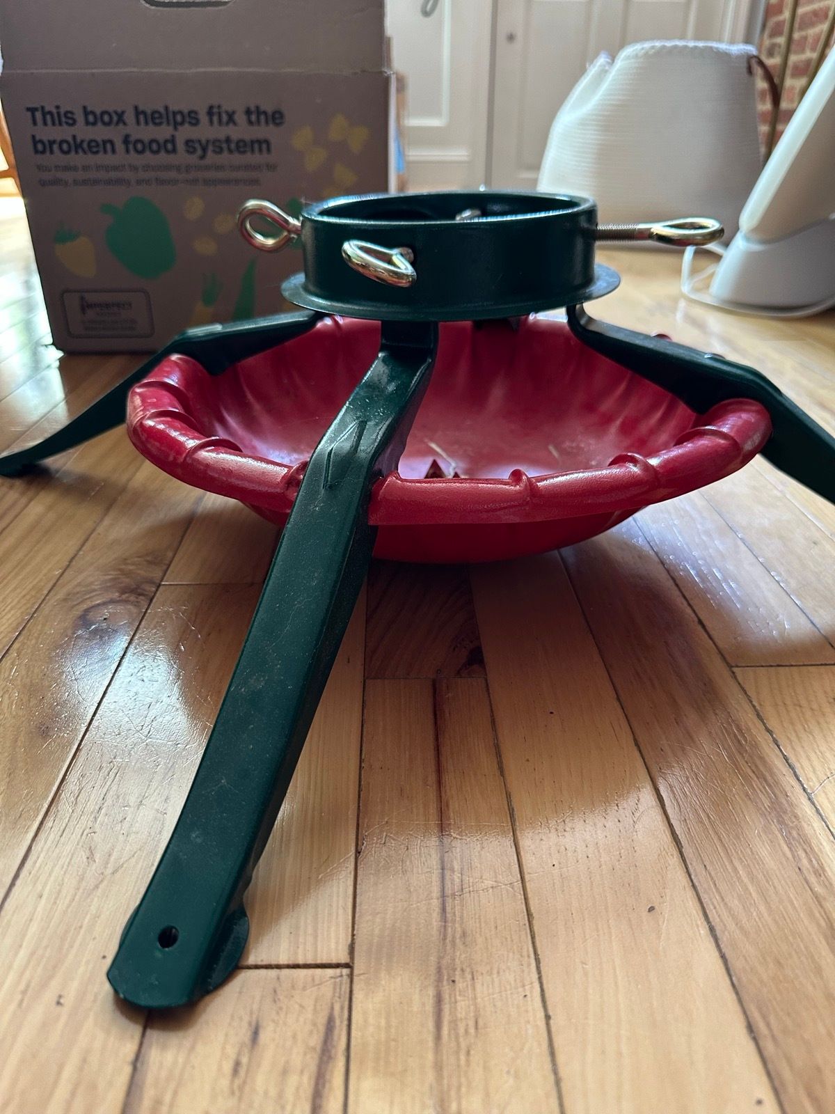 Red and green plastic Christmas tree stand with bolt clamps and a water reservoir.