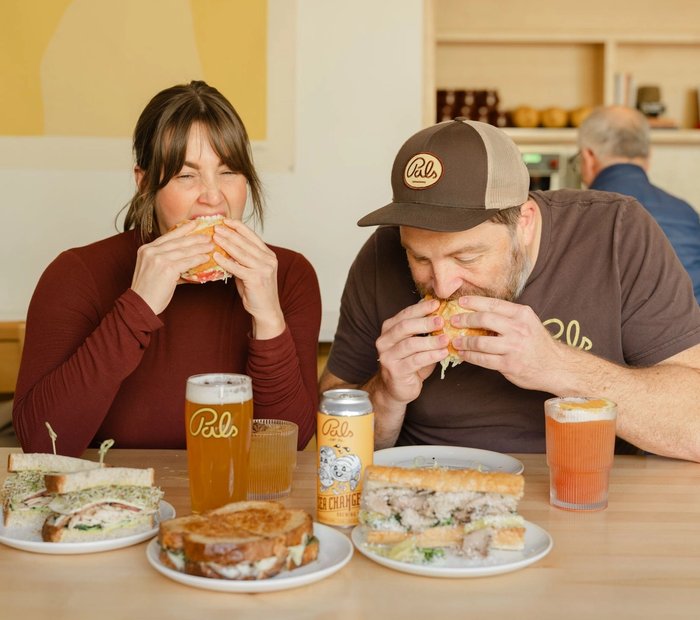 Two people enjoying sandwiches and drinks at Pals Sandwiches in Old Strathcona