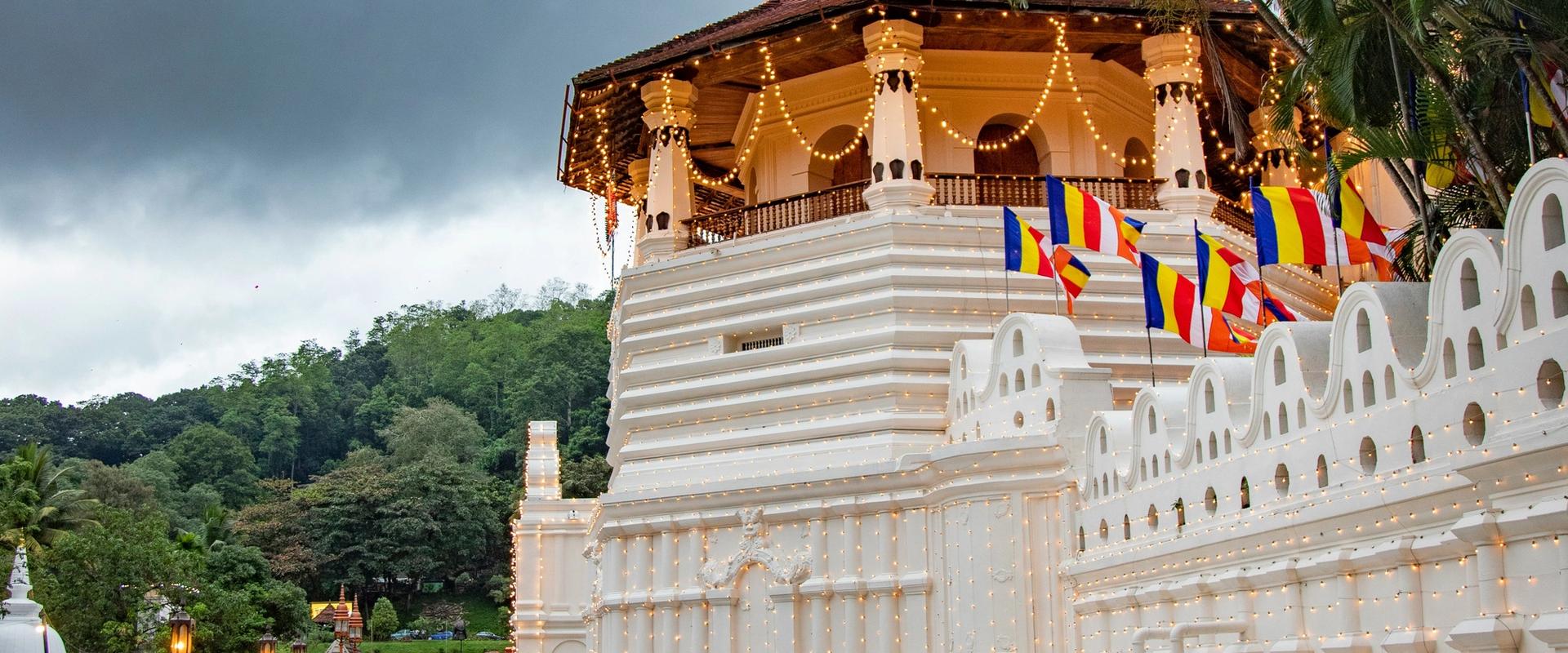 Temple of the Sacred Tooth Relic with Buddhist flags reflected in water in Kandy, Sri Lanka