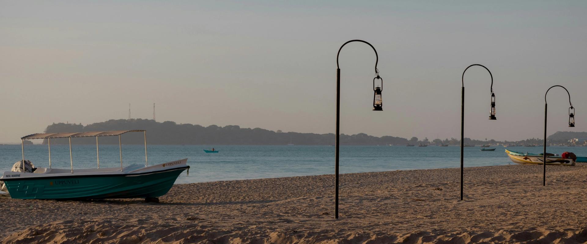 Fishing boat on Trincomalee beach at golden hour with decorative lantern posts, Sri Lanka