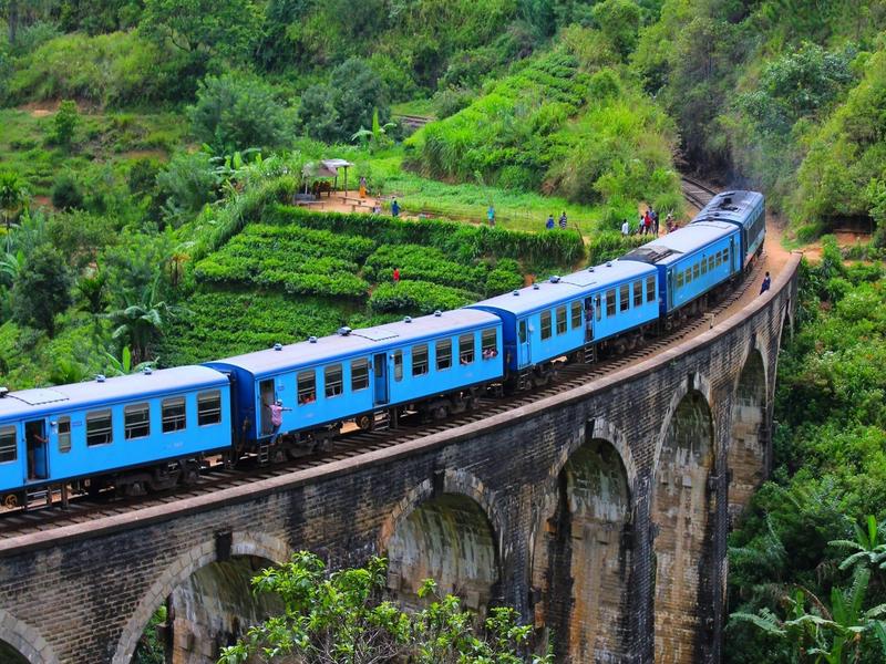 Blue train crossing the Nine Arches Bridge in Ella, Sri Lanka surrounded by lush green tea plantations