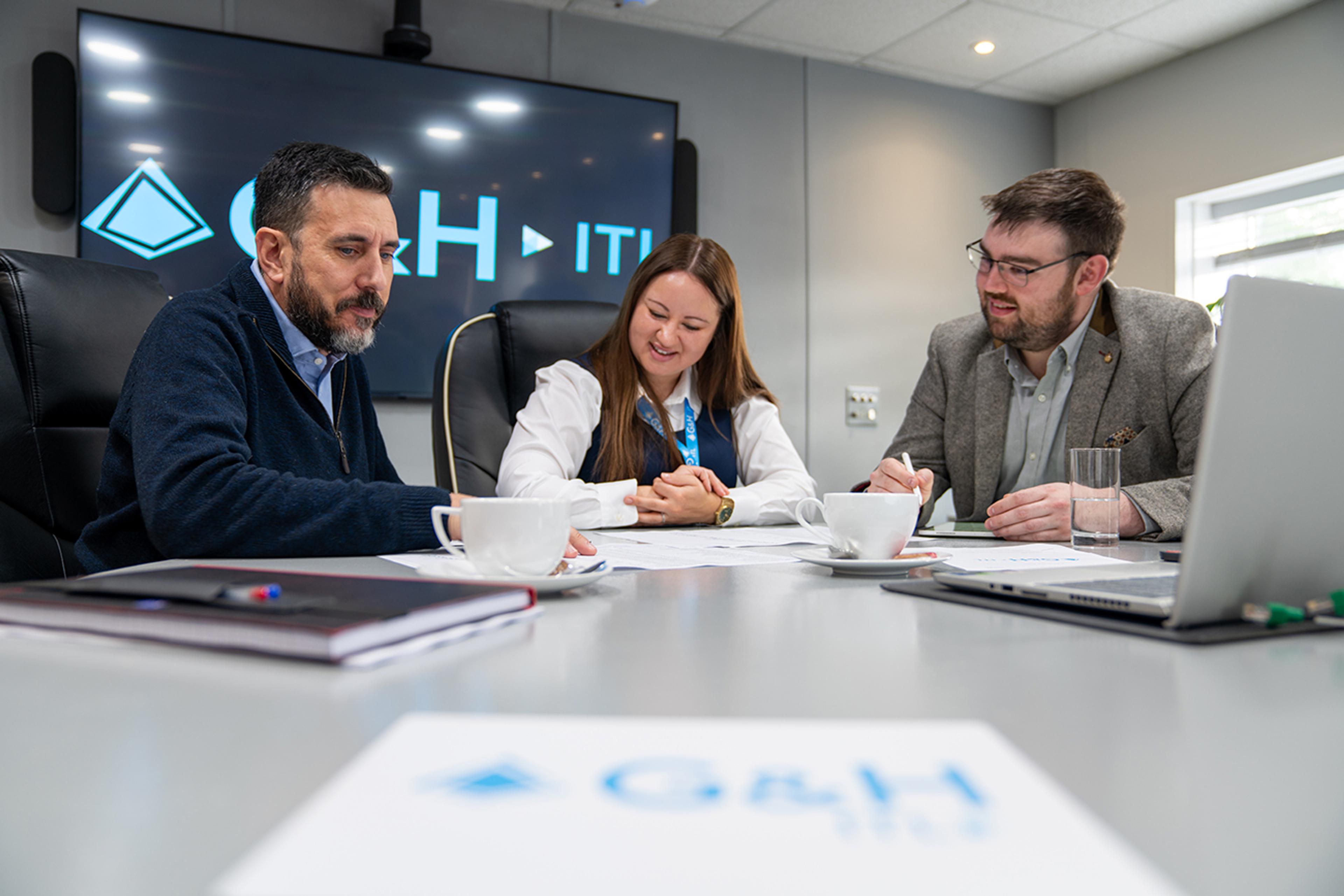 G&H team members conducting pre-manufacturing checks in a meeting room, reviewing technical documents and specifications around a conference table.