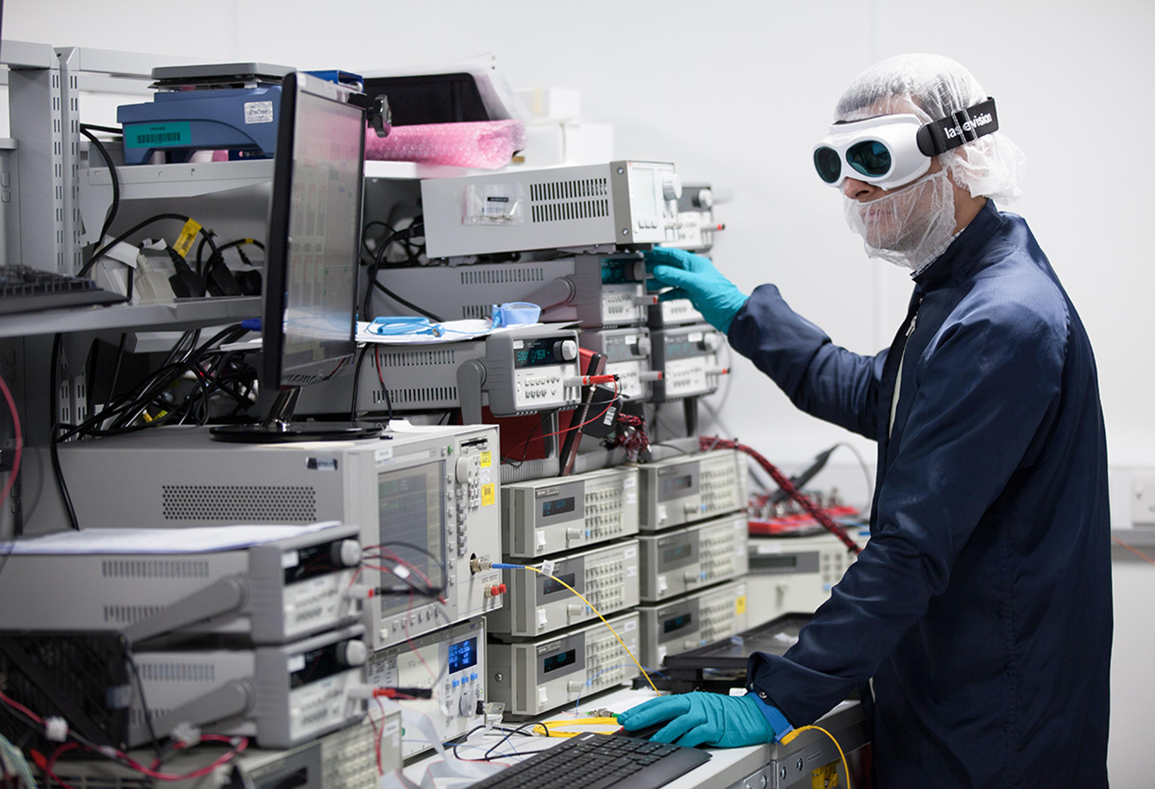 Technician wearing laser safety goggles, gloves and protective clothing, operating laboratory test equipment at G&H’s Torquay facility.