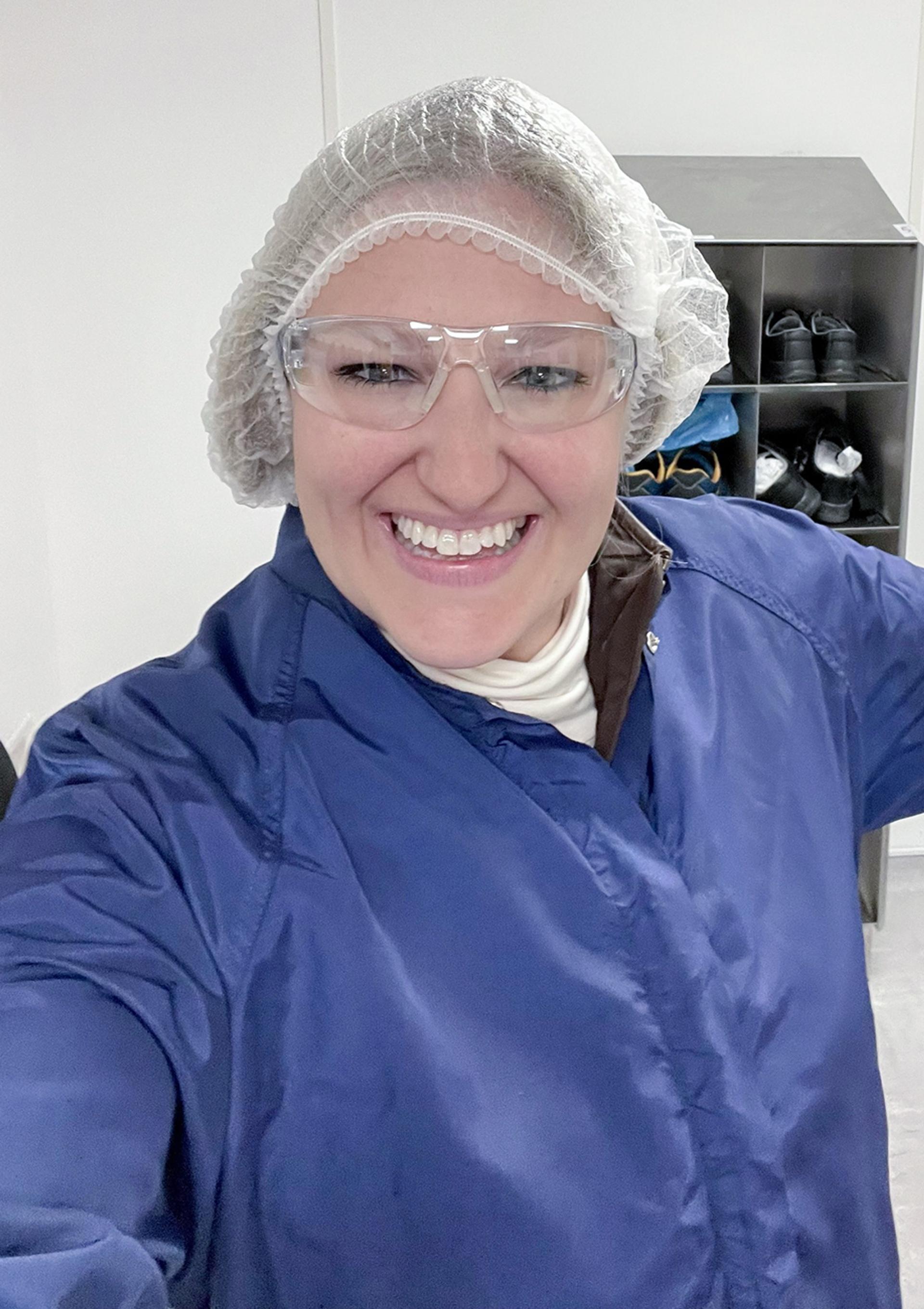 Brittany Ryan smiling during a visit to G&H Torquay, wearing a blue protective coat, hairnet and safety glasses.