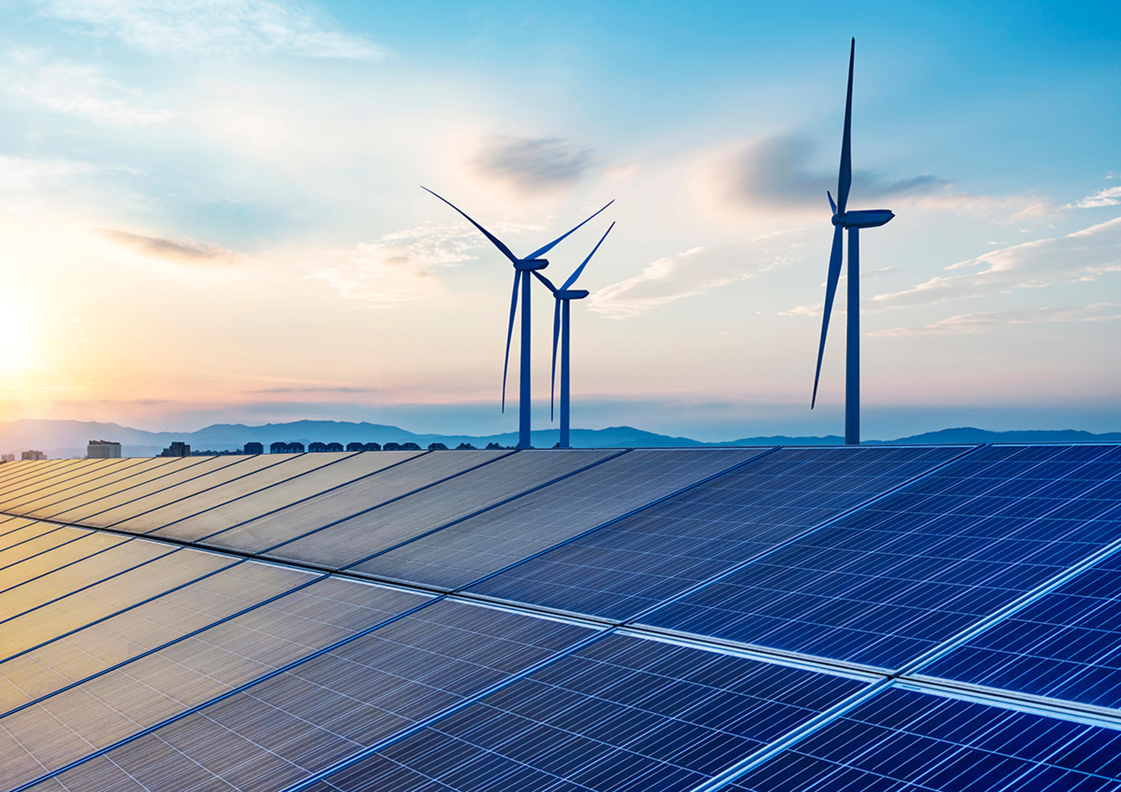 Solar panel array and wind turbines in a landscape at sunrise, representing renewable energy generation.